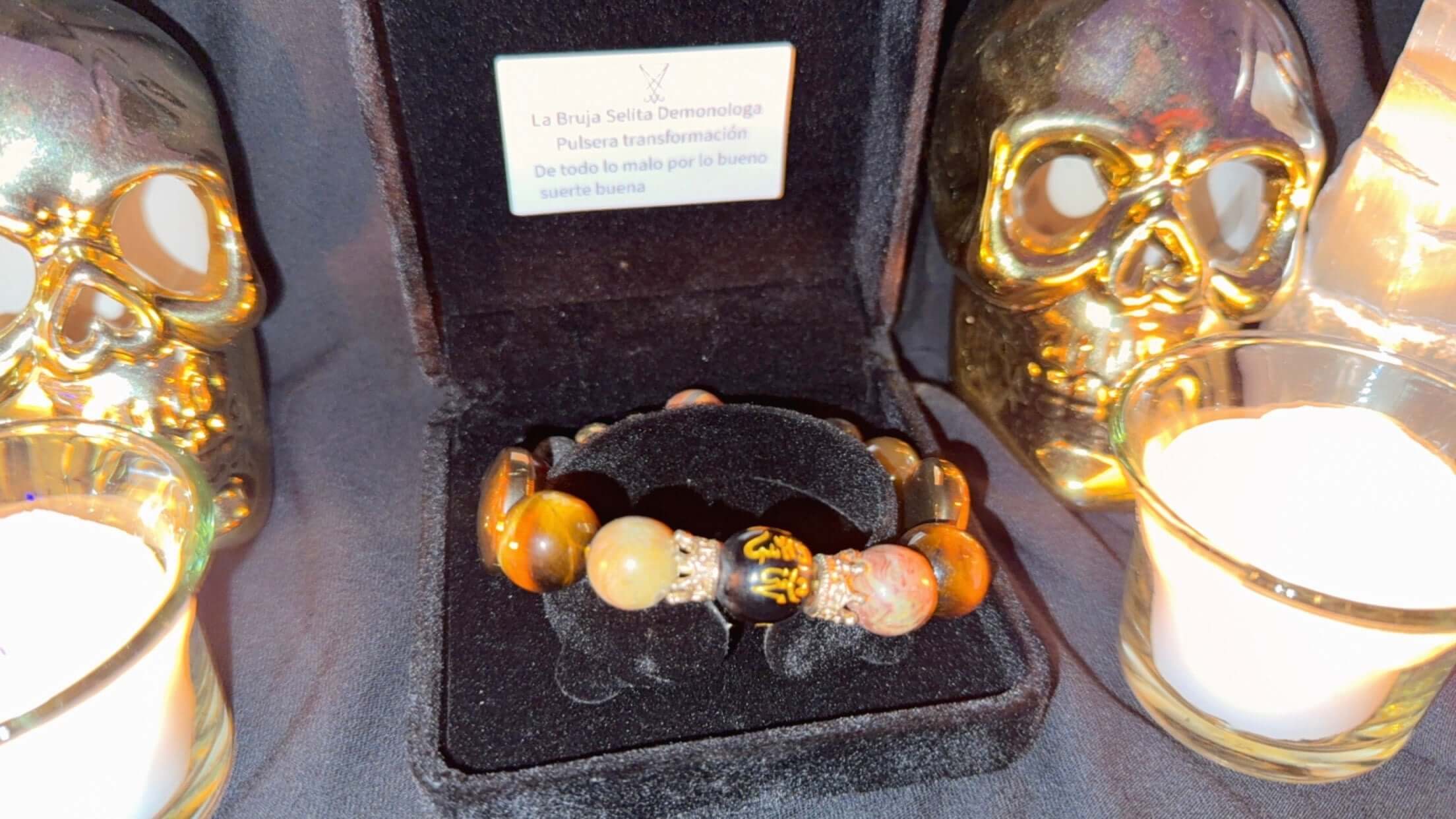 PULSERA DE TRANSFORMACION CON LUCIFER & CHORONZON en una caja negra con calaveras doradas y velas.