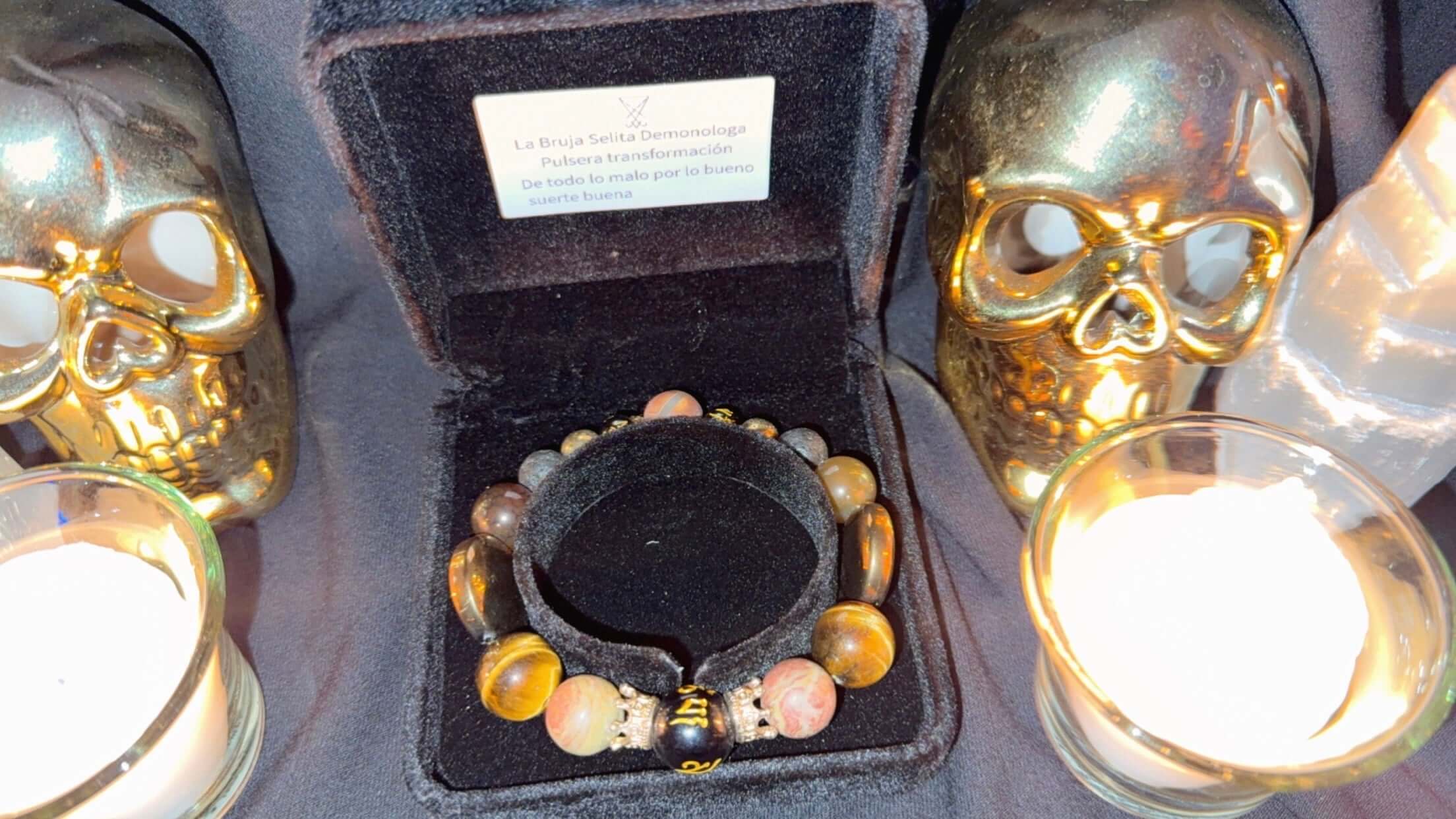 Pulsera de transformación con Lucifer & Choronzon presentada entre calaveras doradas y velas.